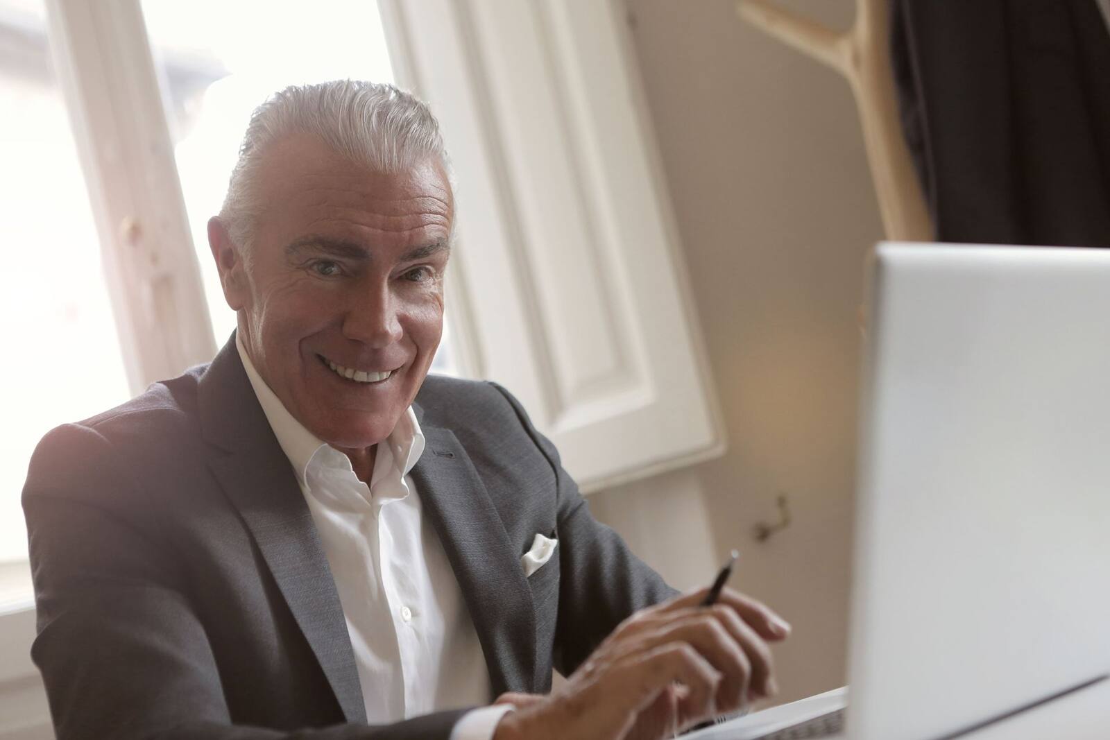 A business professional smiles while working at a laptop in a sunlit office