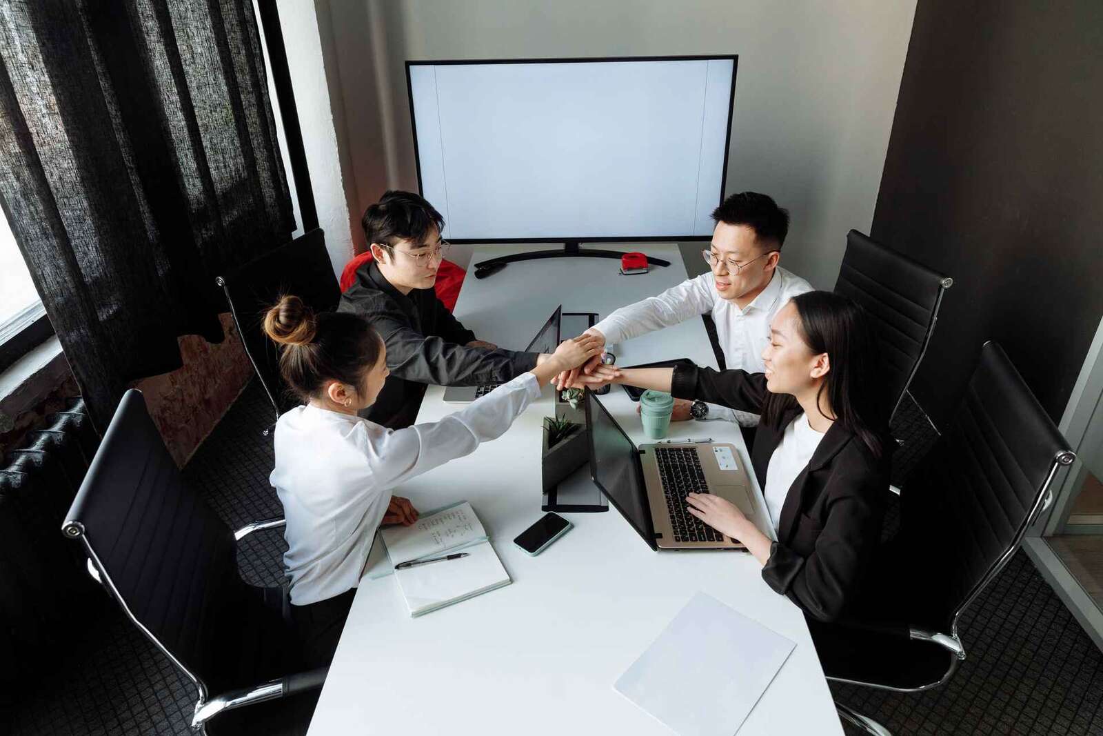 A team stacks hands together over a conference table in a gesture of shared success