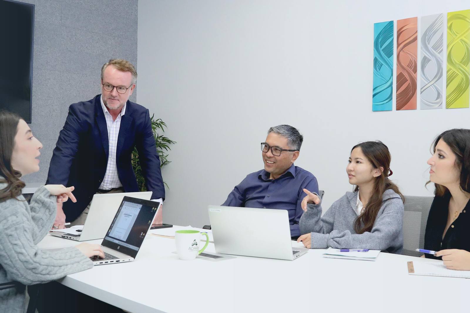 Five ADARx Pharmaceuticals employees around a conference table with laptops in the company's San Diego office, mid-discussion.