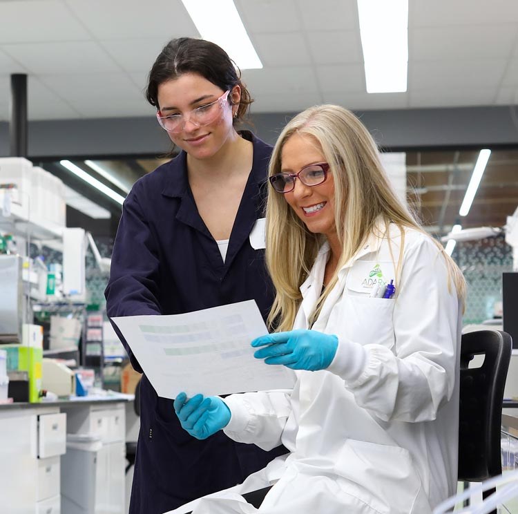 Two ADARx scientists in the company's laboratory, one in an ADARx-branded lab coat, reading a printed data sheet together.