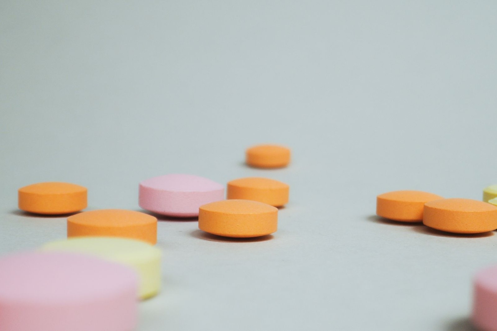 Loose orange, pink, and yellow tablets scattered across a light gray surface, softly out of focus