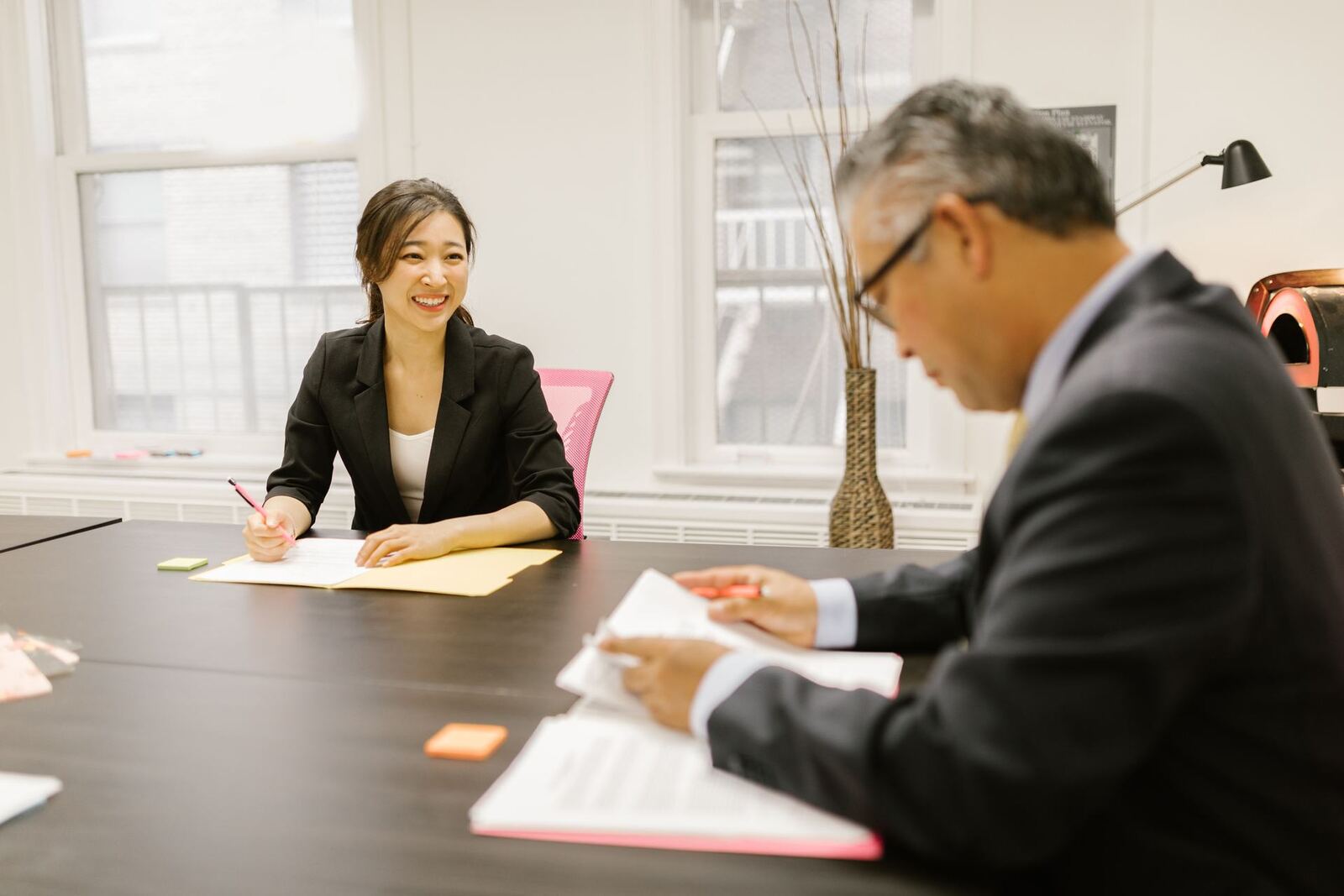 Two colleagues review and sign paperwork together at an office table