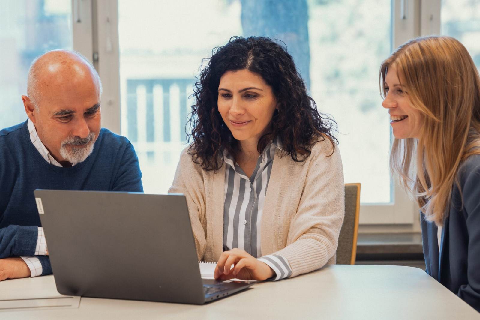 Three AnaCardio team members reviewing work together on a laptop at a table in the company's bright office