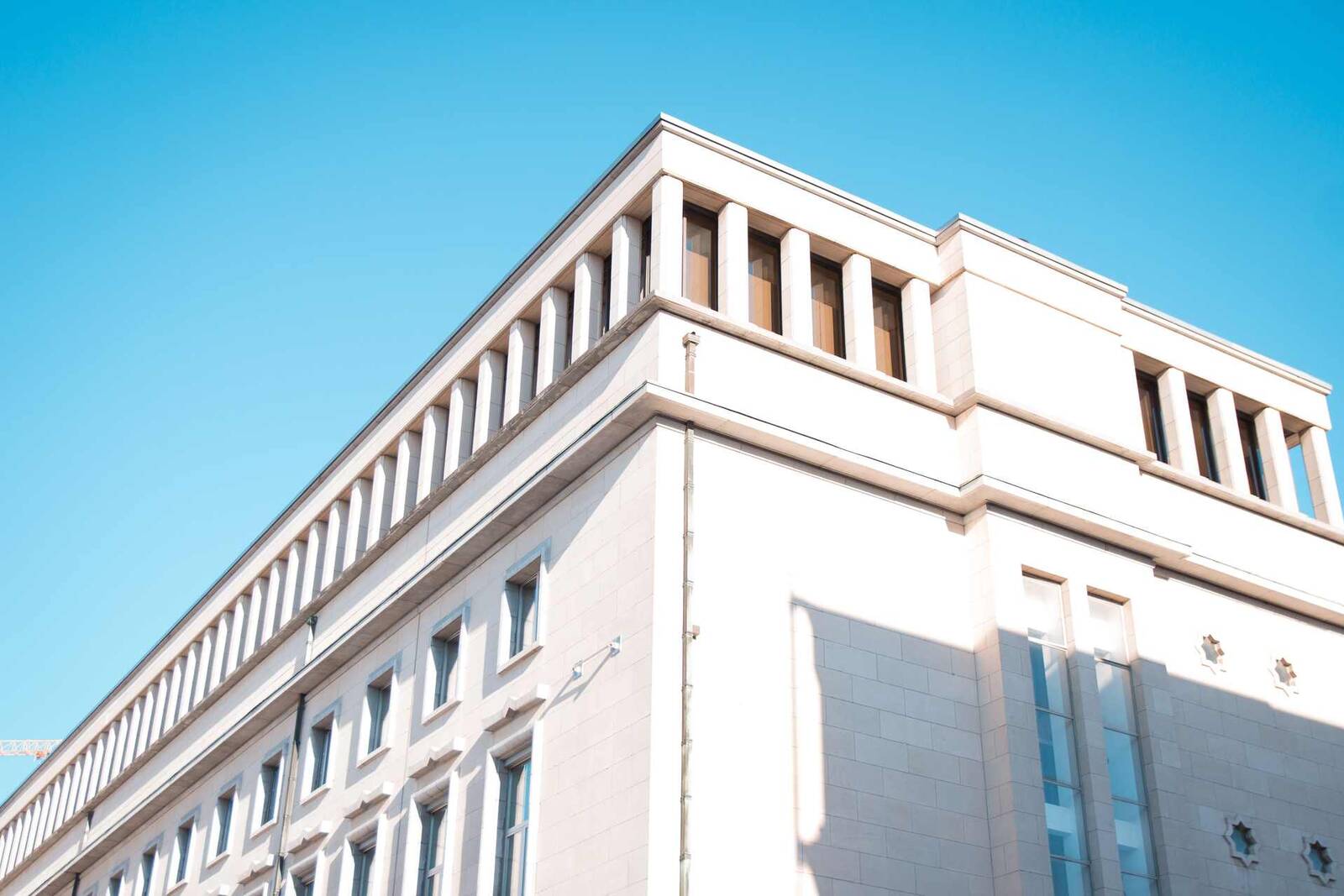 A white institutional office building photographed from below against a clear blue sky