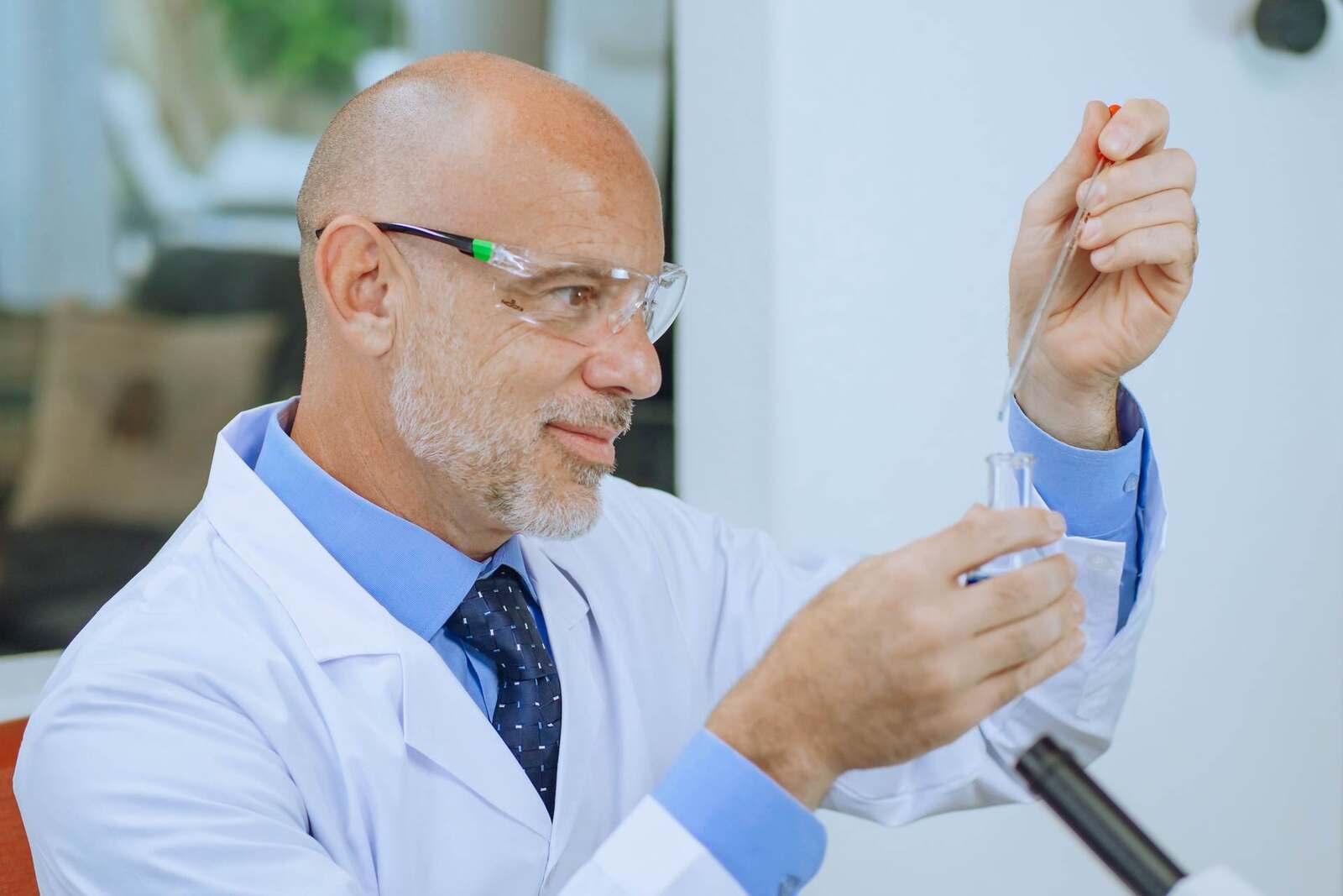 A senior scientist in a tie uses a pipette with a test tube in a bright lab, standing in for the biologic evidence behind Anktiva's label expansion
