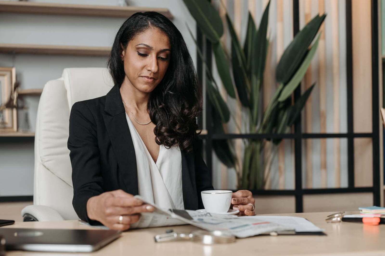A businesswoman in a blazer reads a newspaper over coffee at her desk, a generic stand-in for a company reviewing its own regulatory news