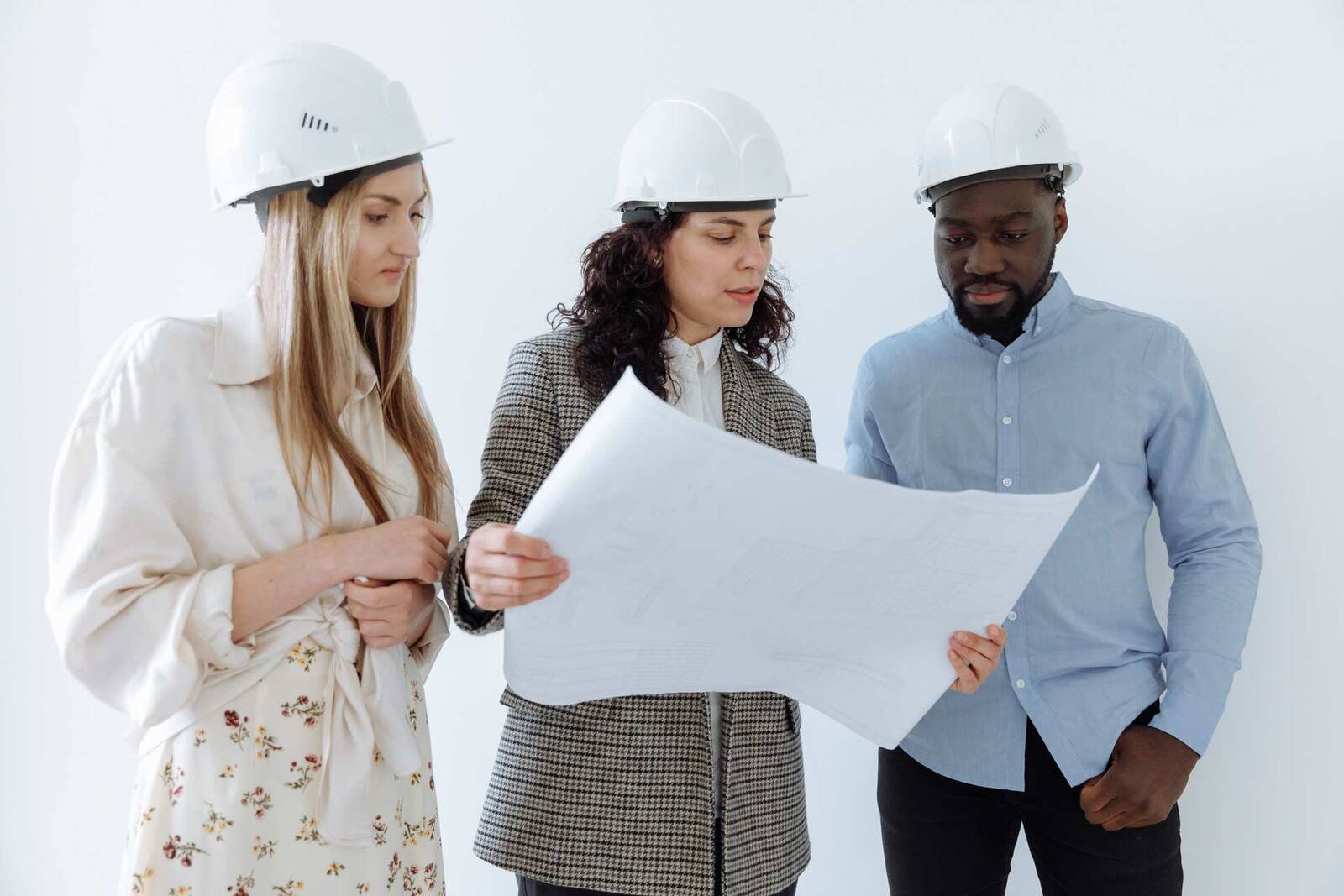 Three professionals in hard hats reviewing facility plans, a generic stand-in for a manufacturing-site inspection or remediation review — not Baxter's own staff or plant