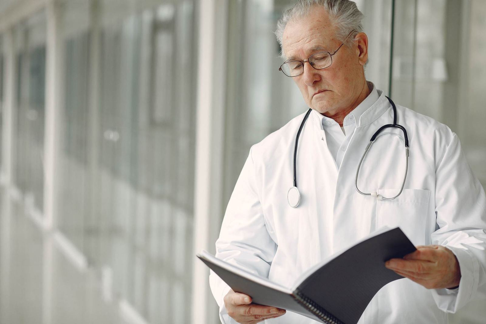 A senior physician in a white coat reads clinical notes in a hospital corridor
