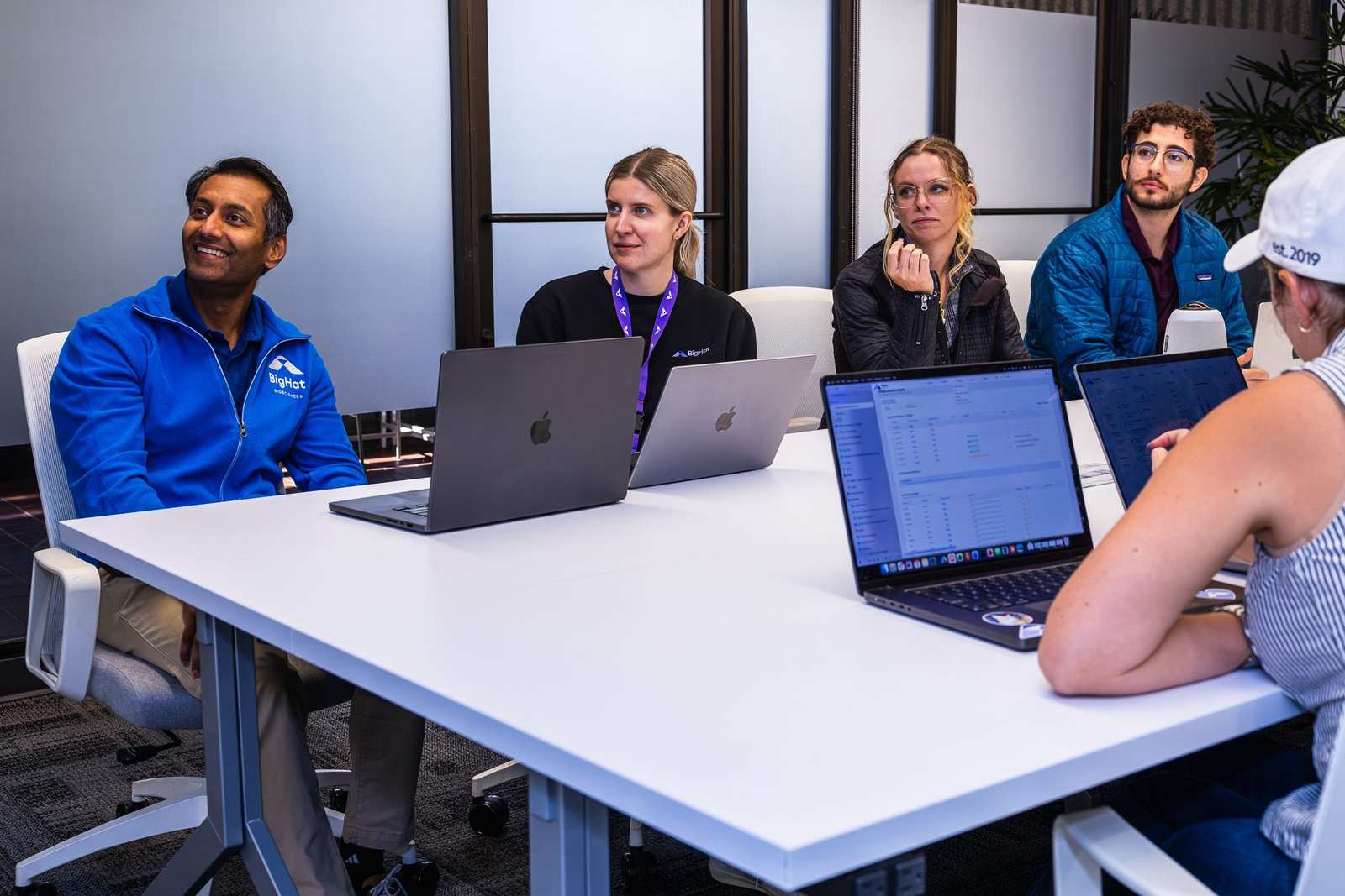 BigHat Biosciences team members in company fleeces sit around a white conference table with open laptops during a meeting at the company's offices