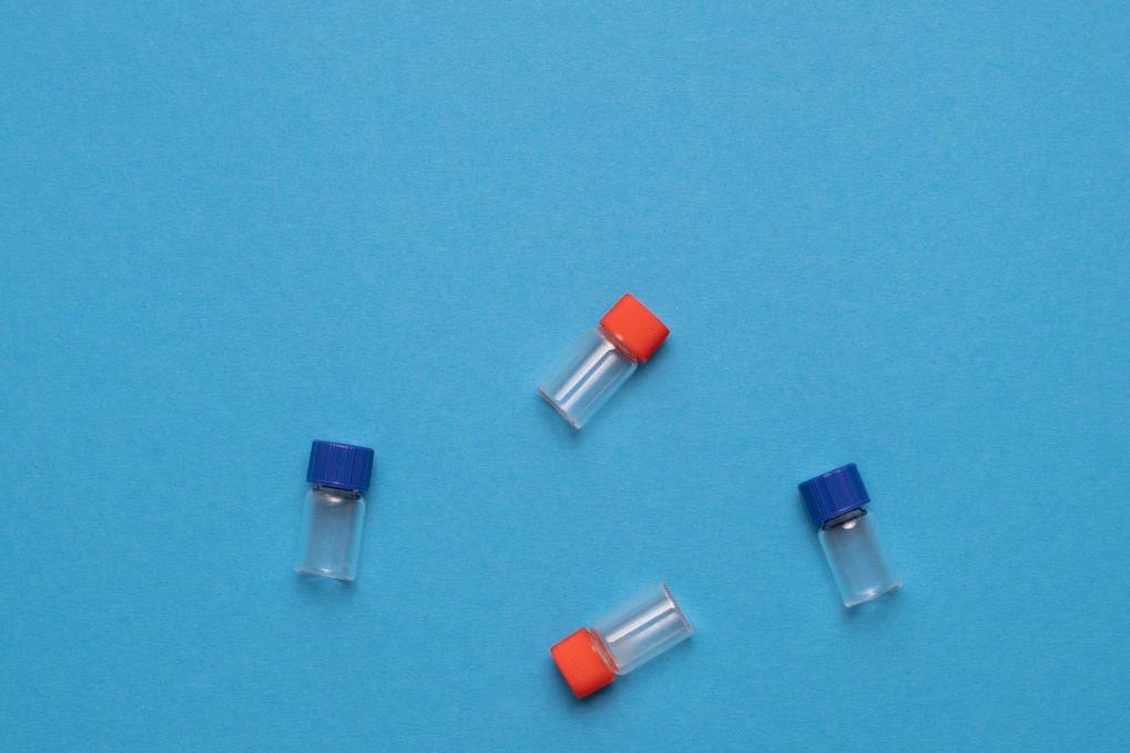 Four small glass vials with red and blue caps scattered across a blue background