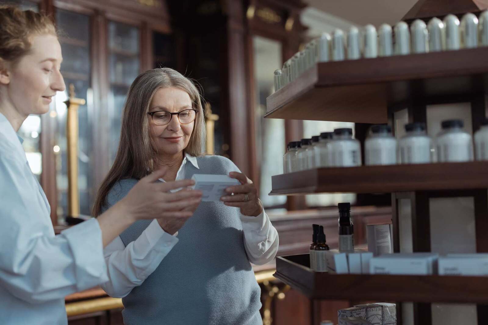 A pharmacist and a customer examine a medication package in a pharmacy
