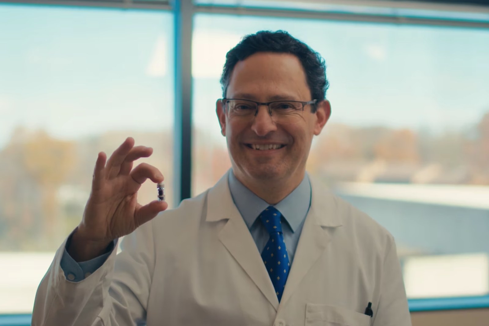 Dr. Jose Derdoy holds a CapsoCam Plus capsule between finger and thumb in a sunlit clinic room