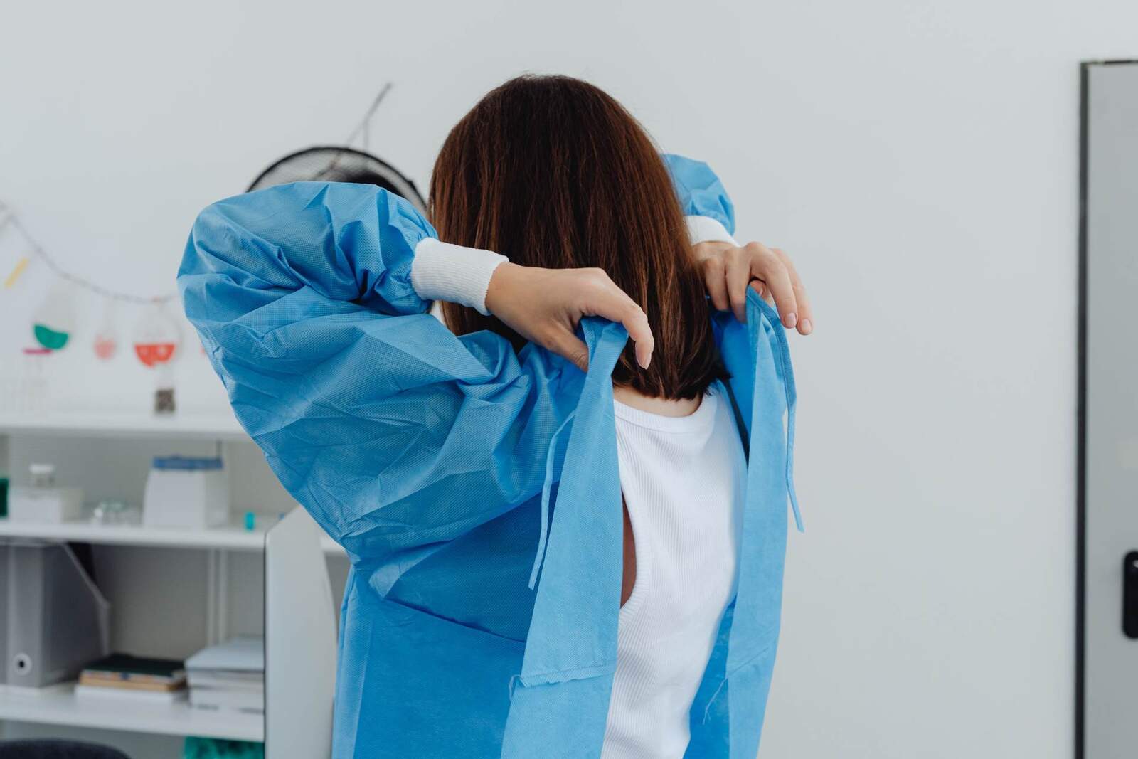 A clinician ties a blue surgical gown in a clinical setting, a generic pre-procedure stand-in