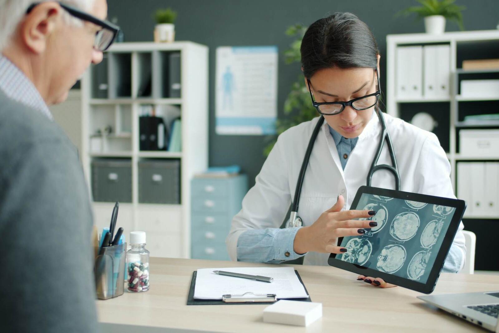 A physician shows a seated patient brain-scan images on a tablet computer