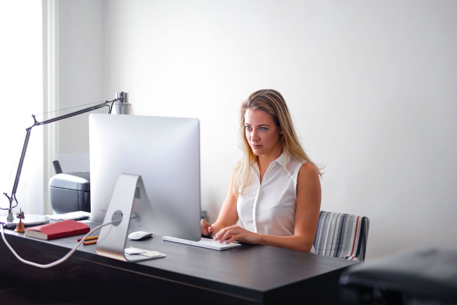A clinician in a white blouse reviews data on a monitor in a bright white office
