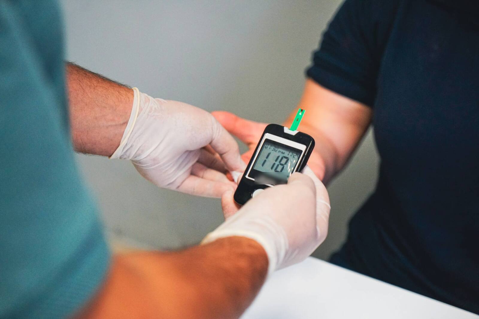 A clinician's gloved hands hold a glucose meter to a patient's fingertip for a point-of-care blood test, a generic stand-in for City Therapeutics' anticoagulation research, not a depiction of its trial site