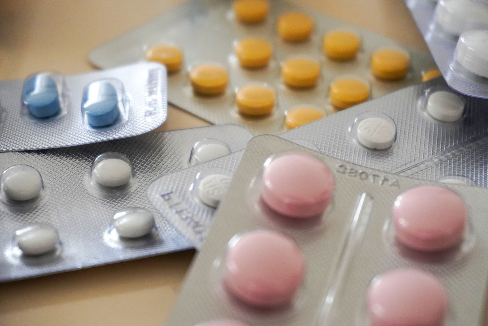 Blister packs holding rows of blue, yellow, white, and pink tablets, viewed close up on a wooden table