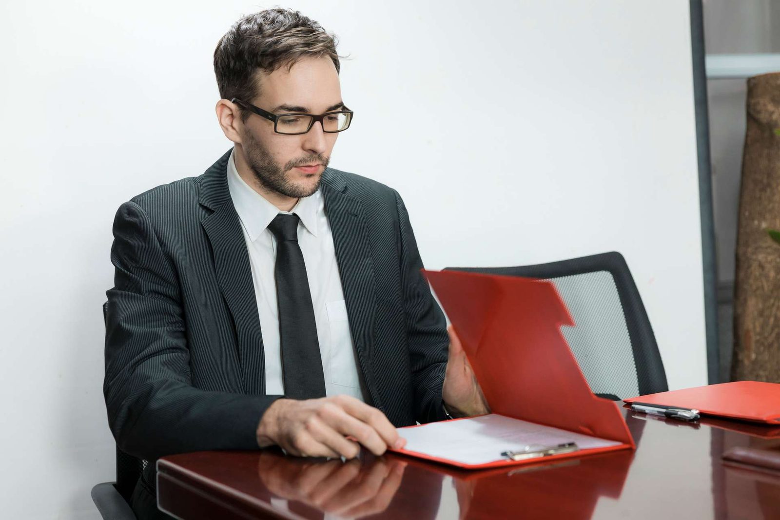 A businessman in a suit reviews a red folder open on a boardroom table