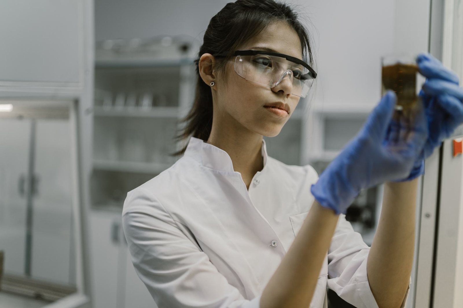 A researcher in safety glasses and blue gloves inspects a laboratory sample in a research facility