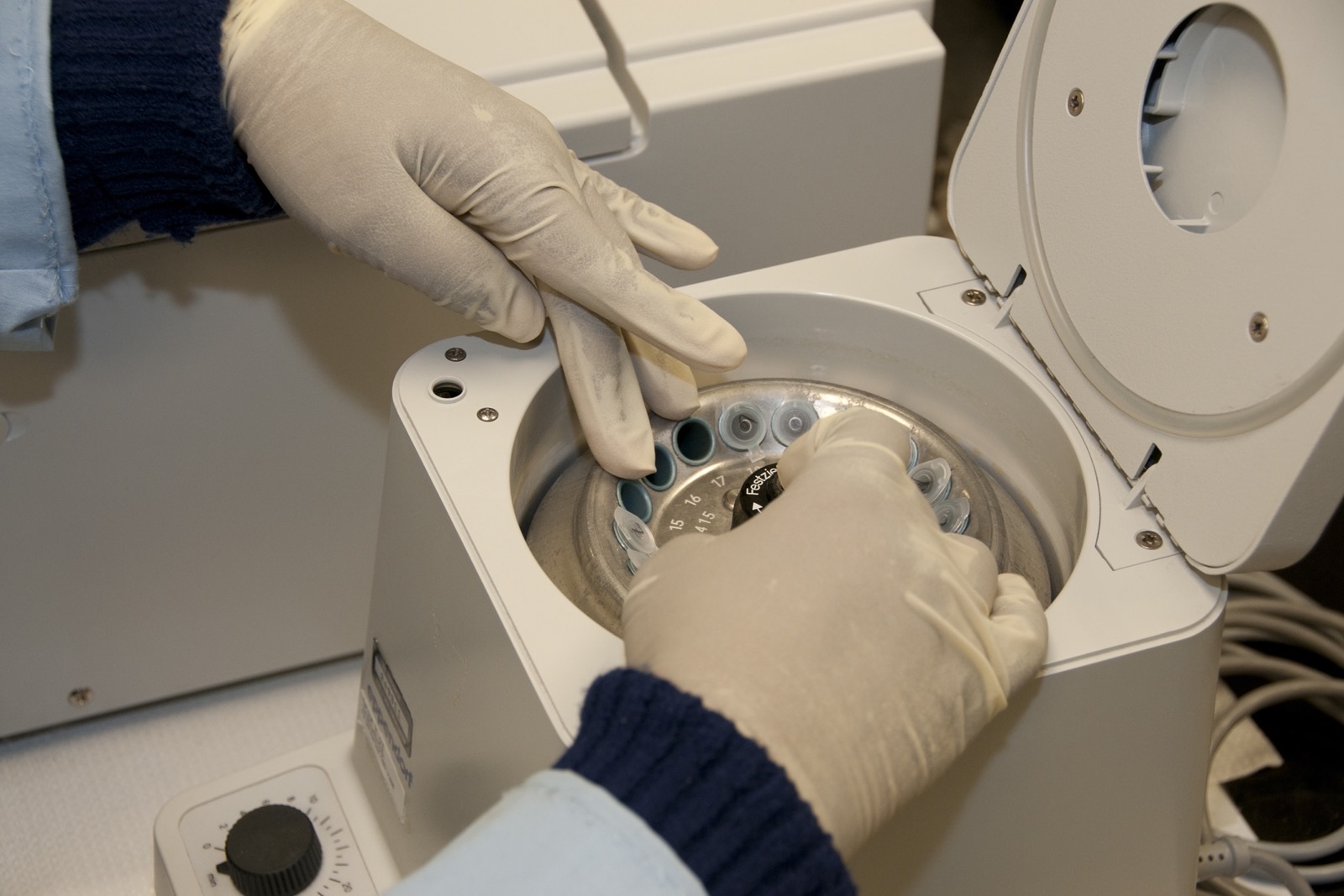 Gloved hands loading sample tubes into a benchtop centrifuge in an FDA laboratory