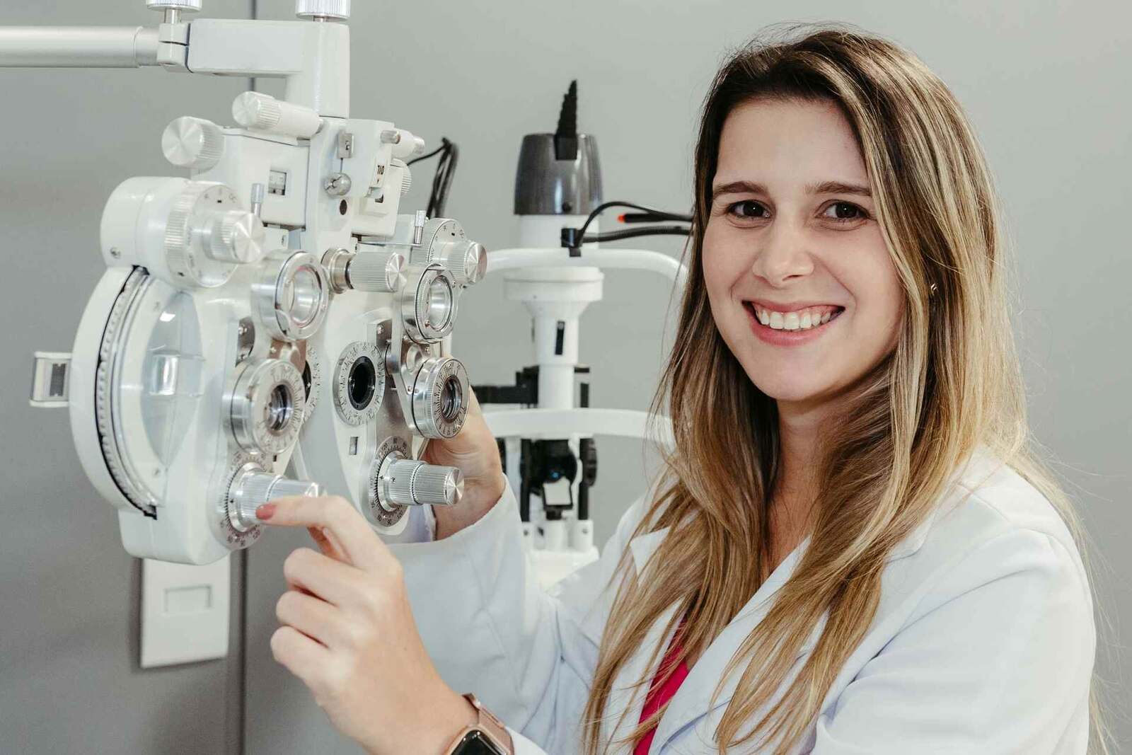 An optometrist shows a patient a phoropter during a vision exam in a bright eye clinic, standing in for the counterfeit eye-drop warning