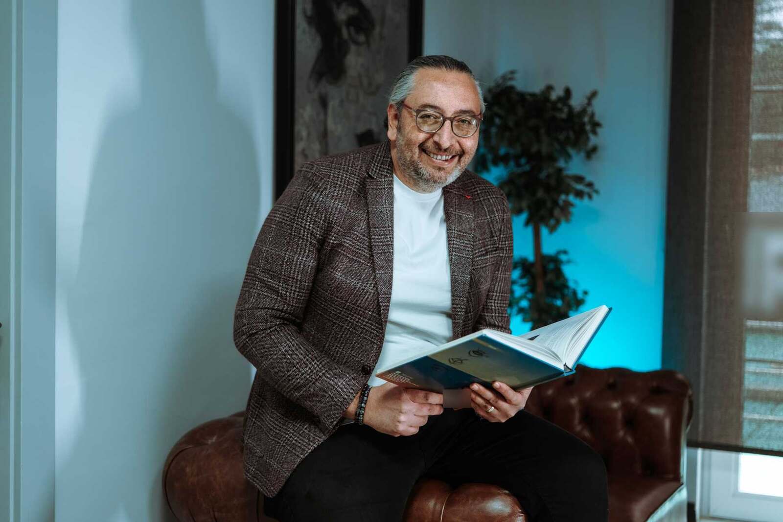 A smiling executive in a plaid blazer reviews a bound document while seated in an office lounge