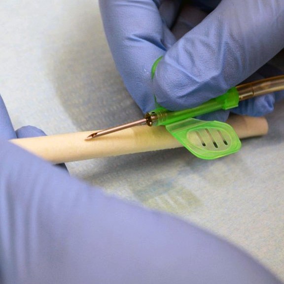 Gloved hands insert a cannulation needle into a length of Silkothane vascular graft on a bench
