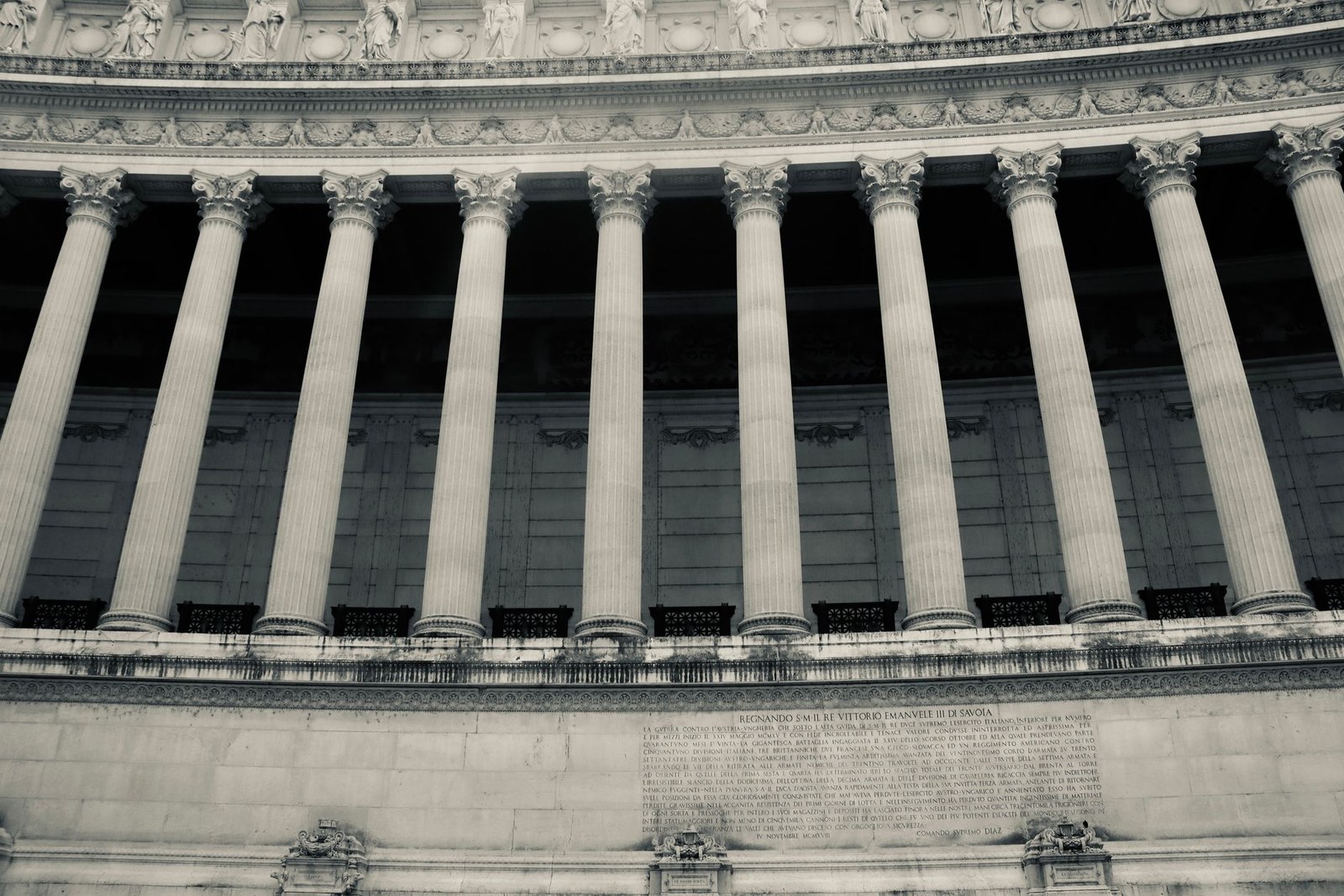 A row of Corinthian columns and classical stone statuary lines the curved facade of a government building
