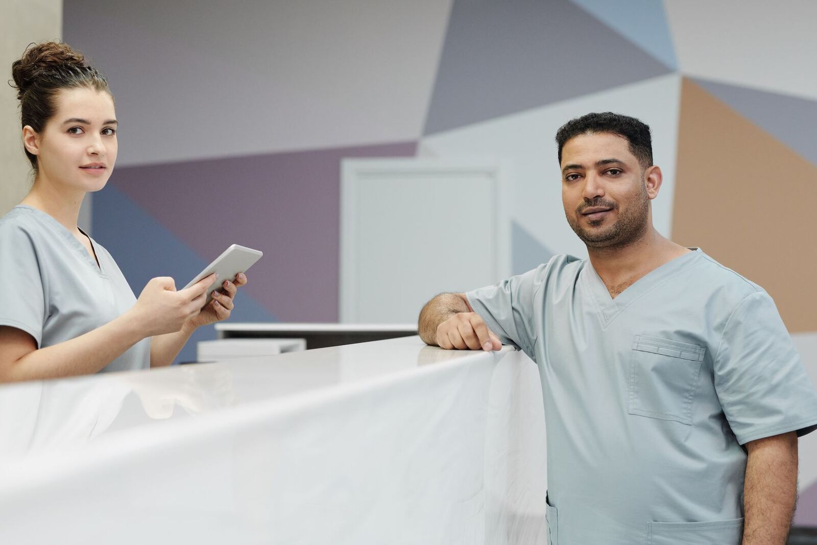 Two clinicians in scrubs confer at a bright hospital reception desk