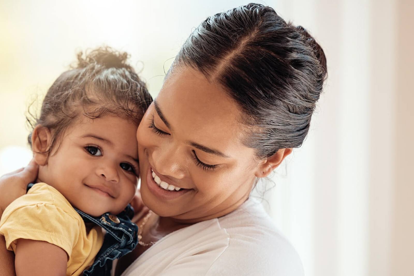 A smiling woman holds a toddler in a yellow shirt close, cheek to cheek, from Edwards Lifesciences' AUTUS valve page