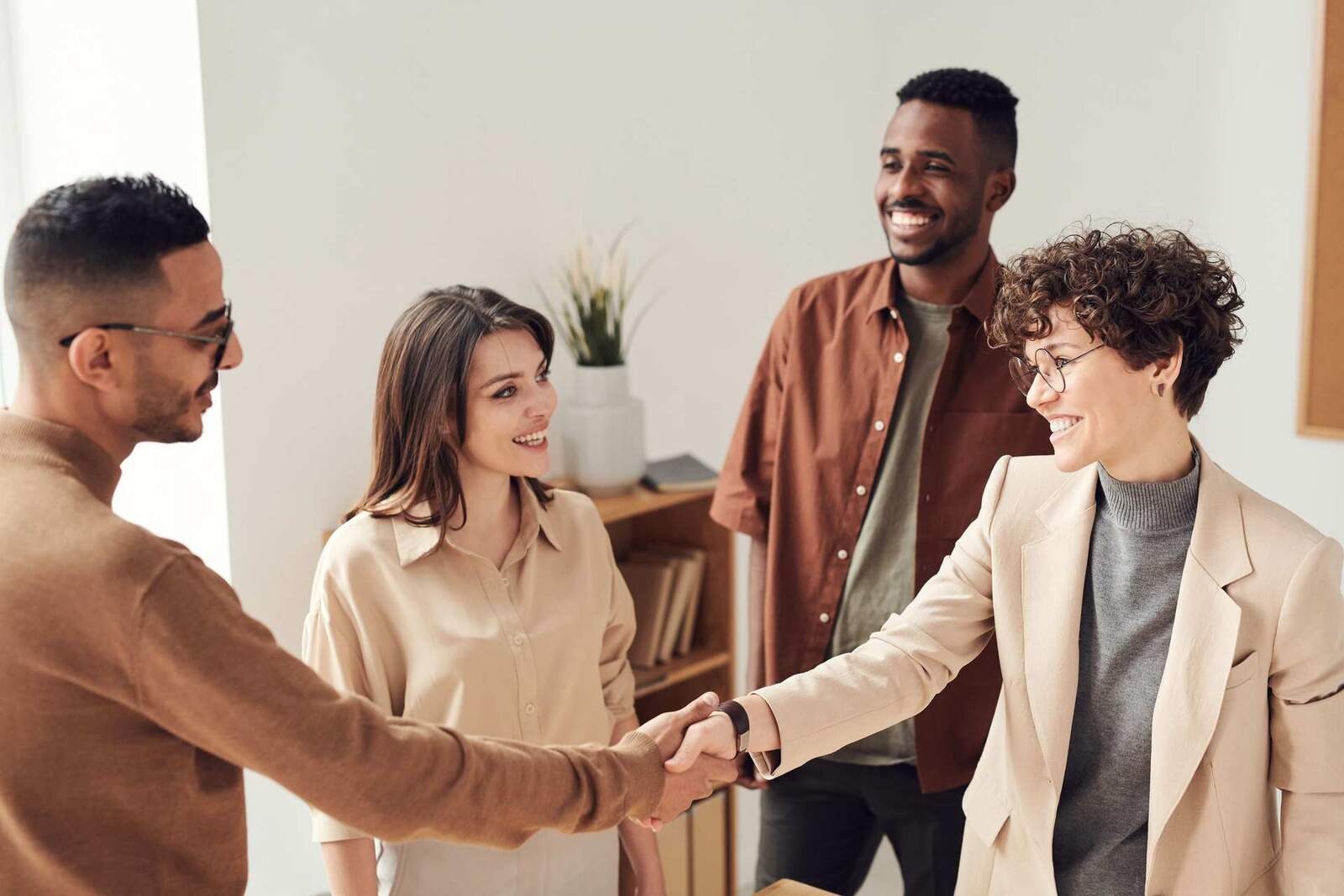 Four colleagues shake hands and smile in a bright office setting