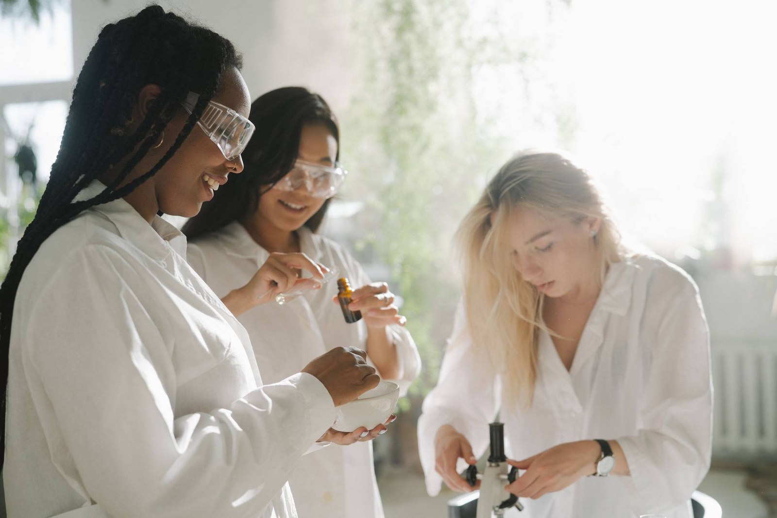 Three scientists in a sunlit lab examine a bottle and a bowl of solution while adjusting laboratory equipment