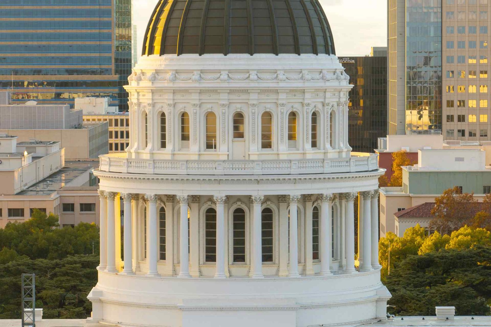A government building dome with classical columns rising above a city skyline at sunset