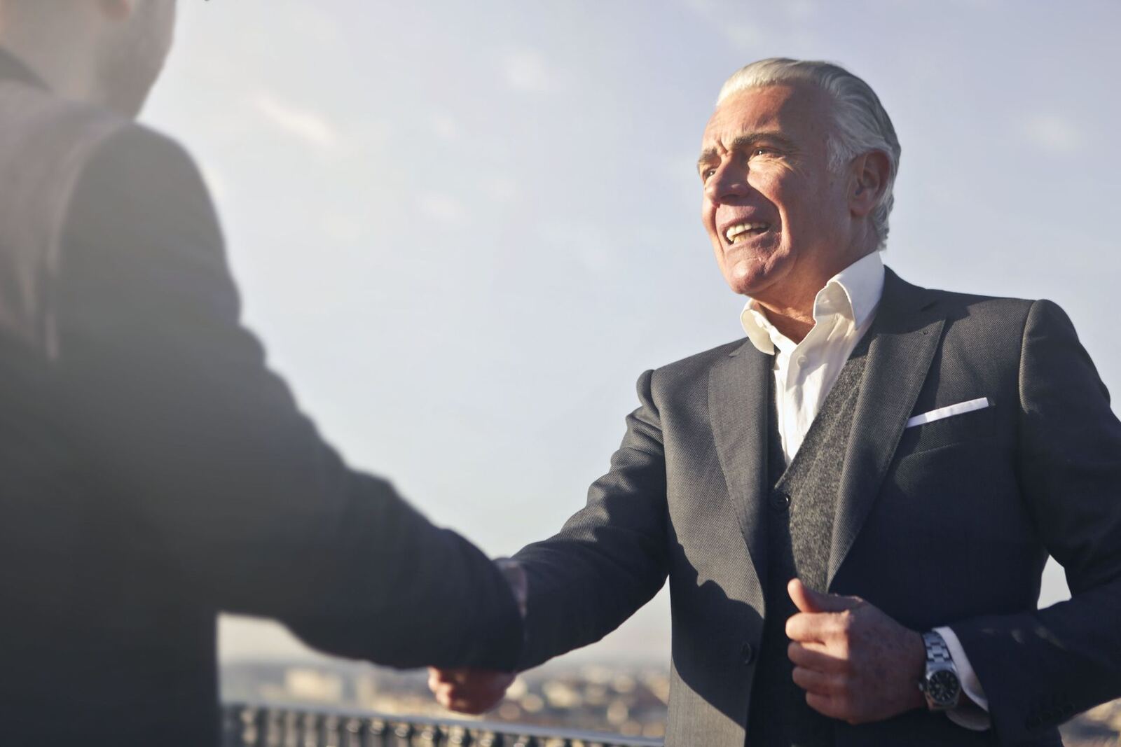Two colleagues shake hands outdoors against a bright sky