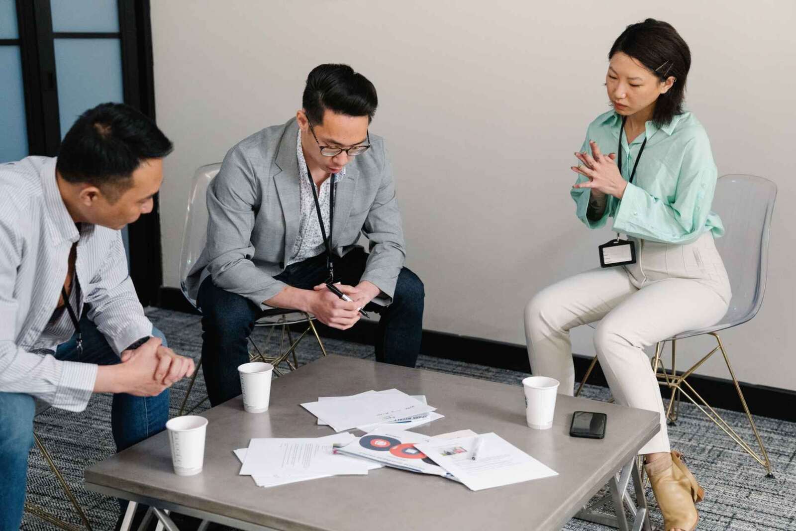 Three colleagues with lanyards review printed documents around a table