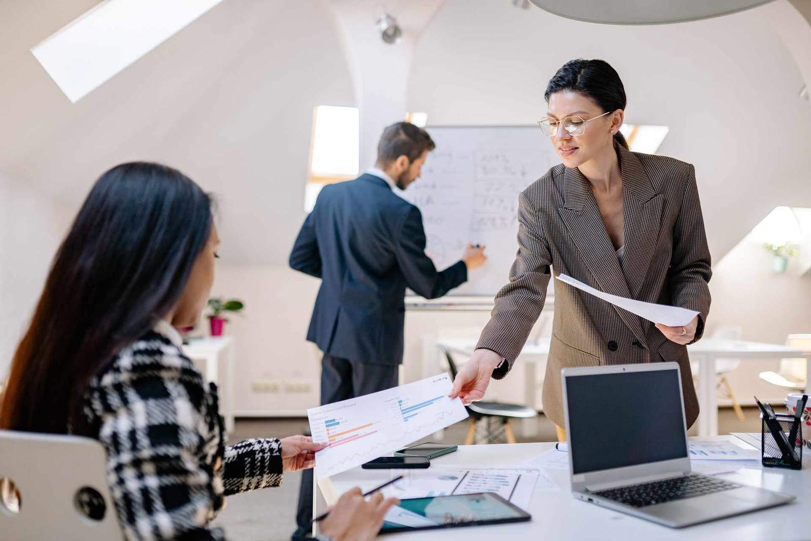 A team of colleagues reviews a chart and hands off a printed report during a planning session in a bright loft office