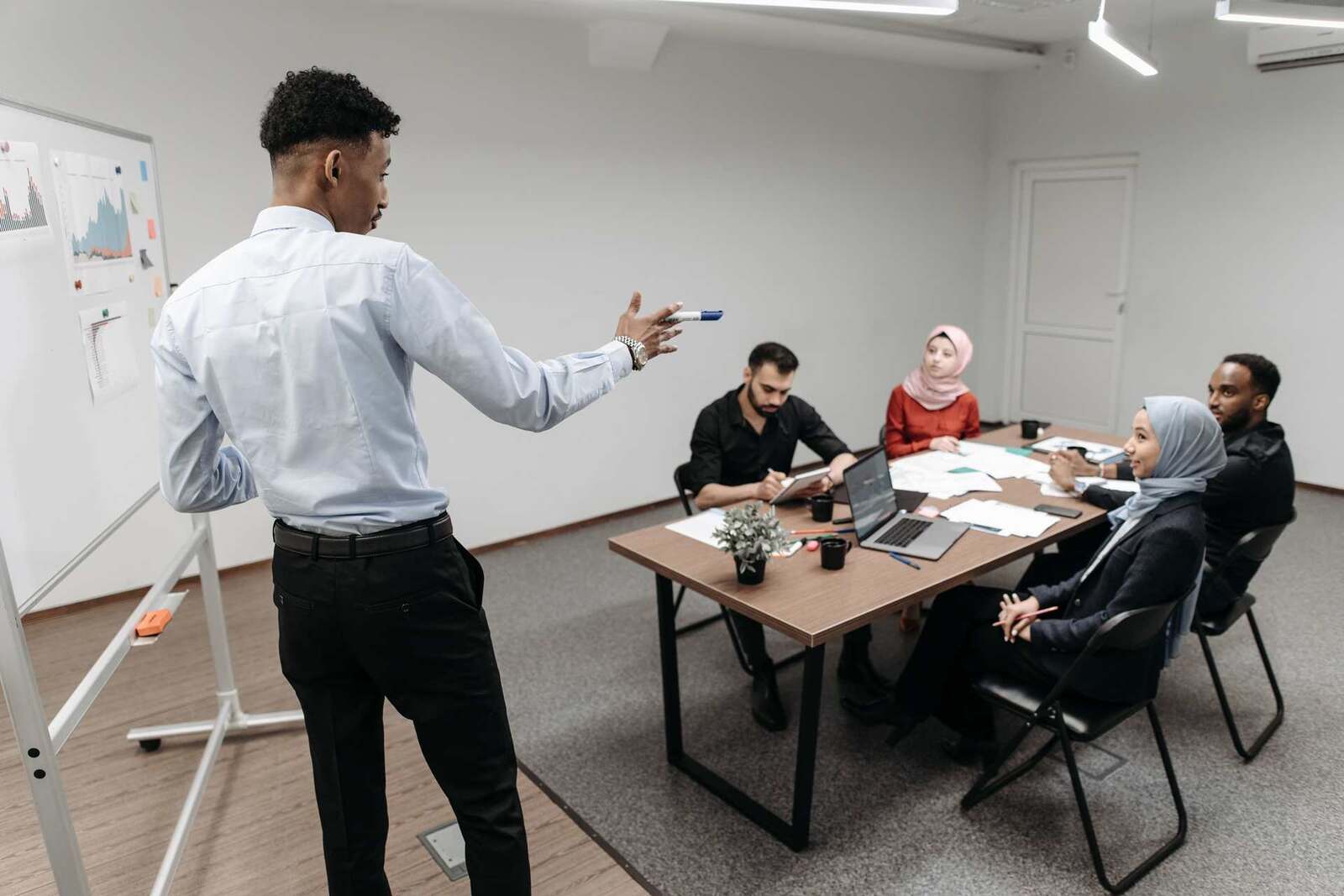 A colleague gestures toward a whiteboard while briefing a seated team