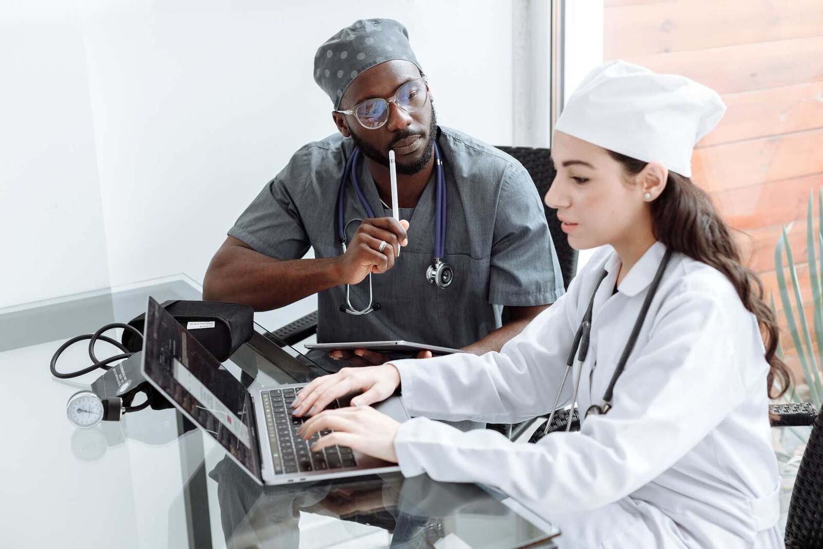 Two clinicians in scrubs review patient data together on a laptop