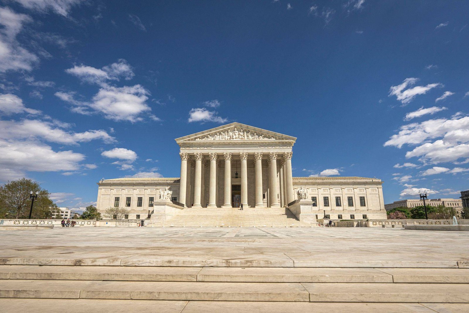 The US Supreme Court building with cherry blossoms and an American flag under a clear blue sky