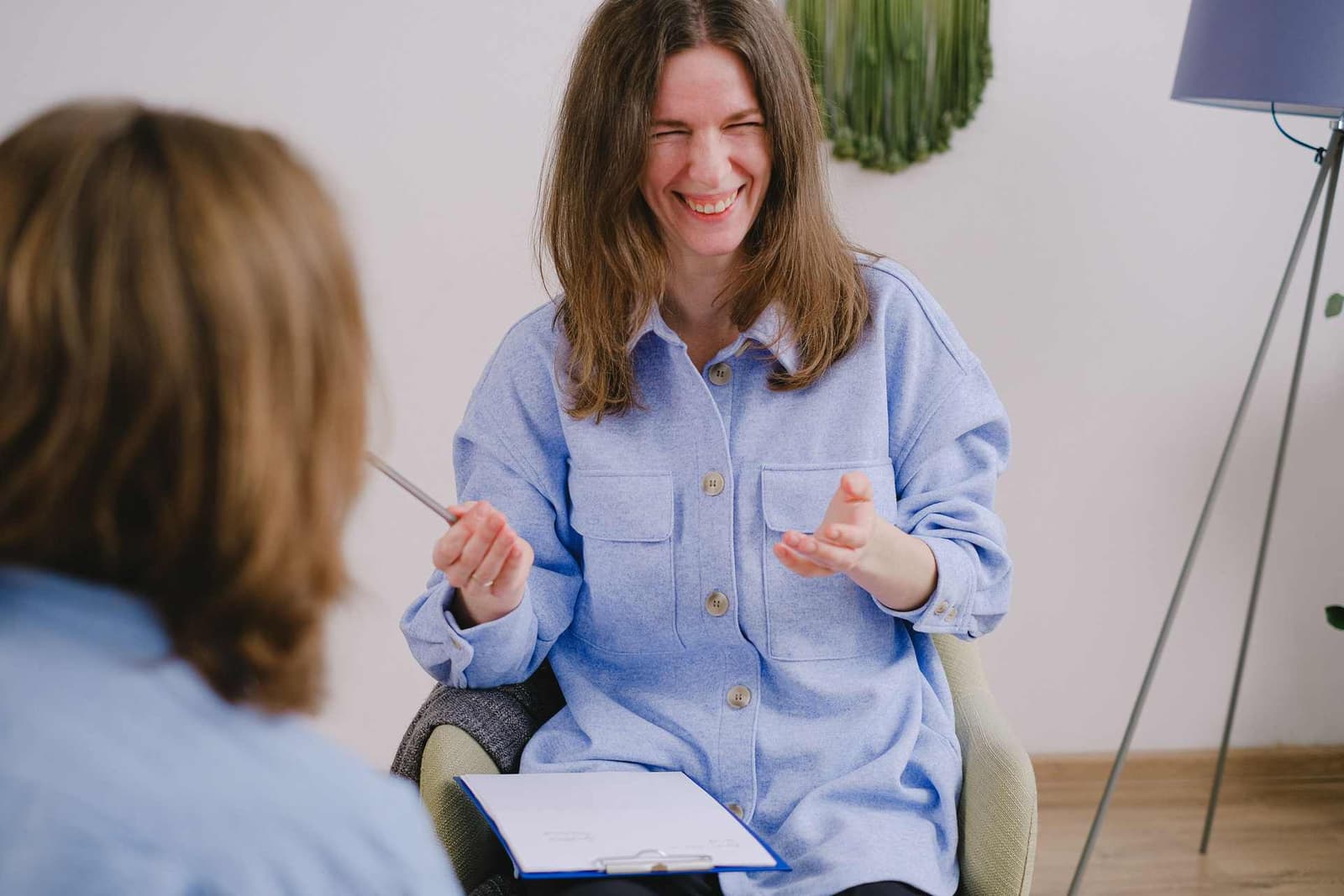 A woman laughs mid-conversation while holding a clipboard during a bright, informal consultation