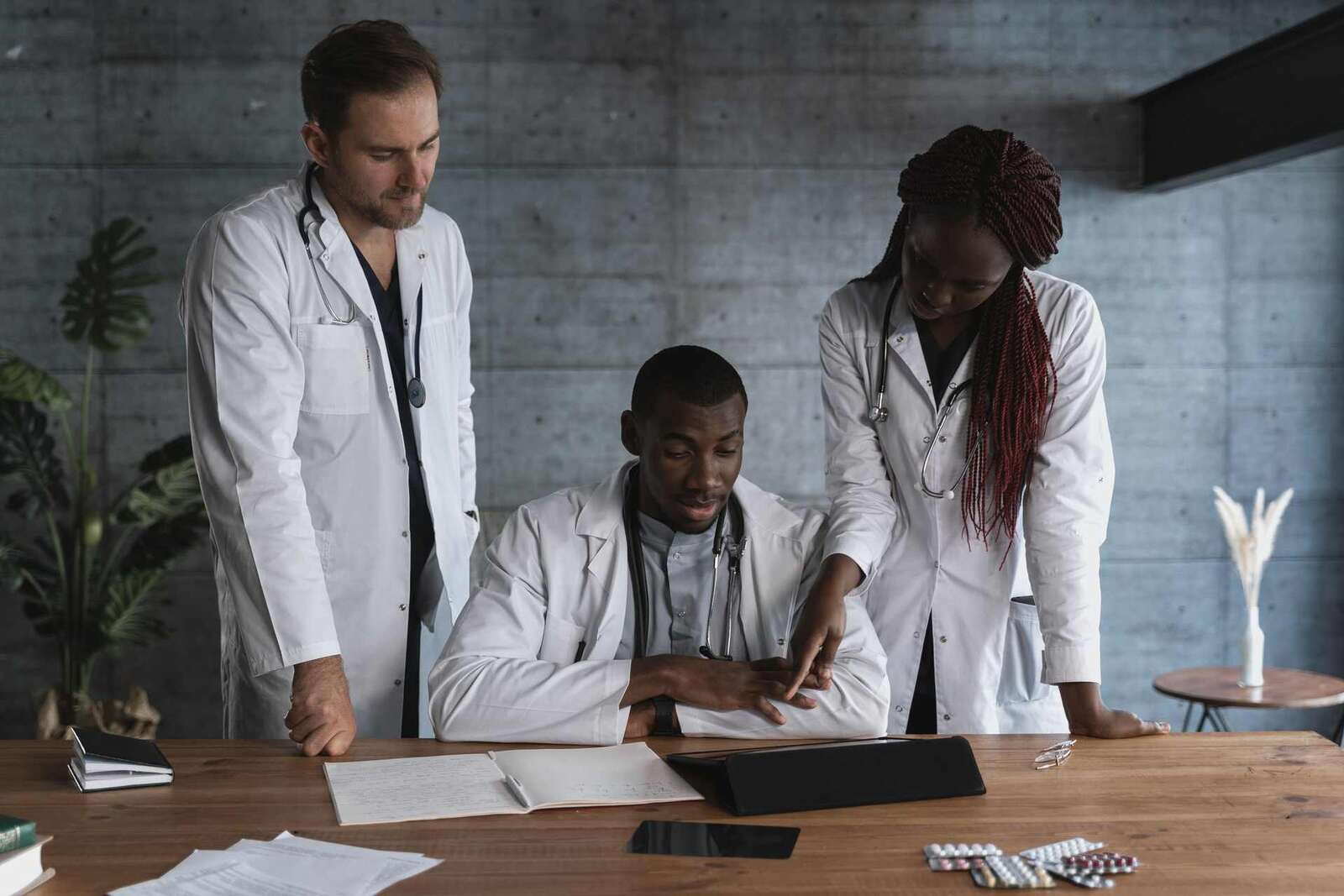 Three physicians in white coats review a patient's chart and medication together at a desk