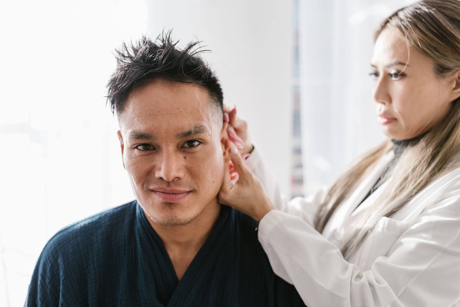 A clinician examines a patient's skin near the hairline in a clinic — a generic stand-in for a skin check, not a psoriasis-specific scene