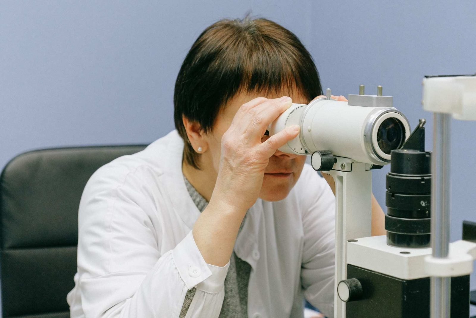 A clinician in a white coat examines a patient at an ophthalmic slit lamp