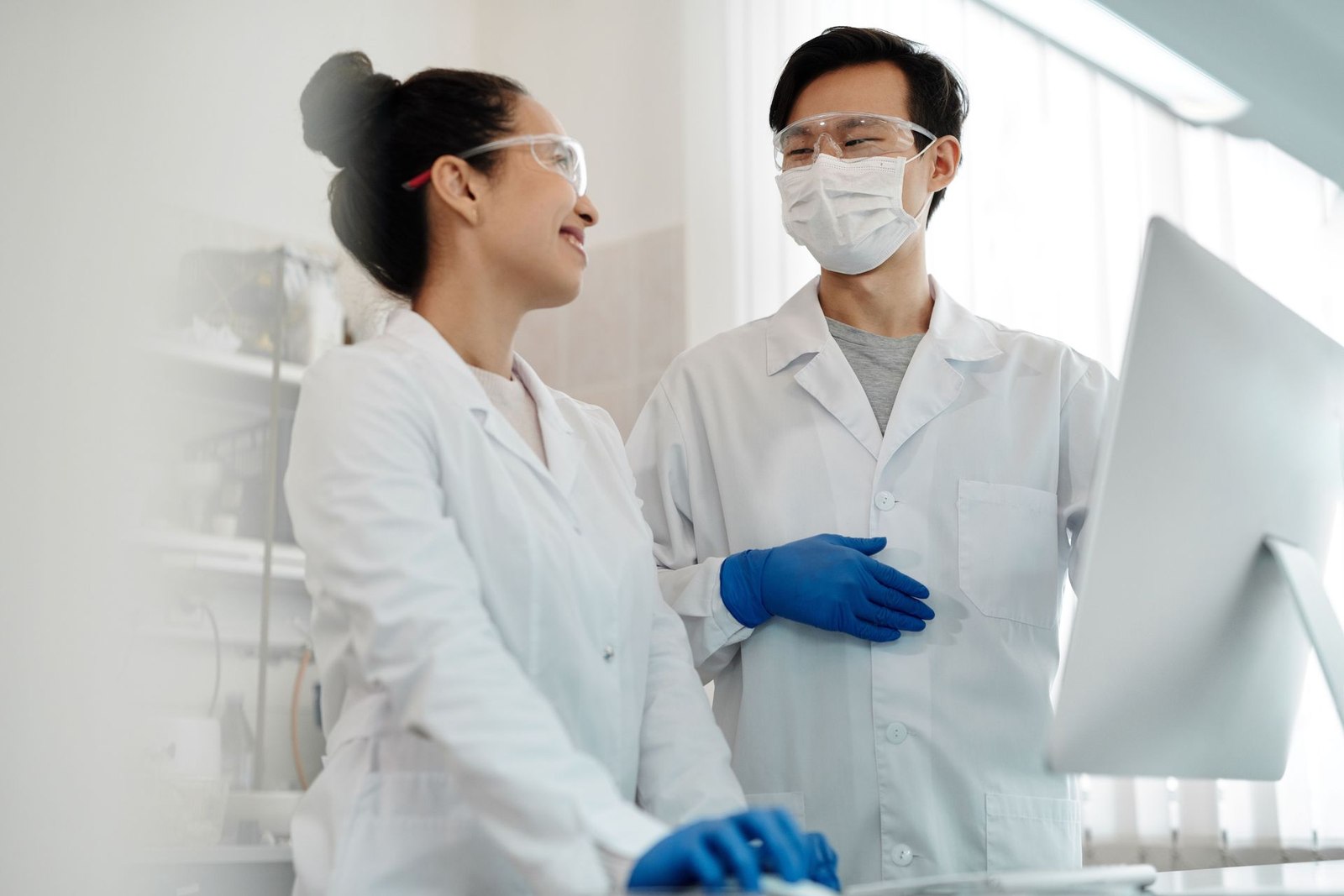 Two researchers in lab coats and safety glasses examining a specimen through a microscope