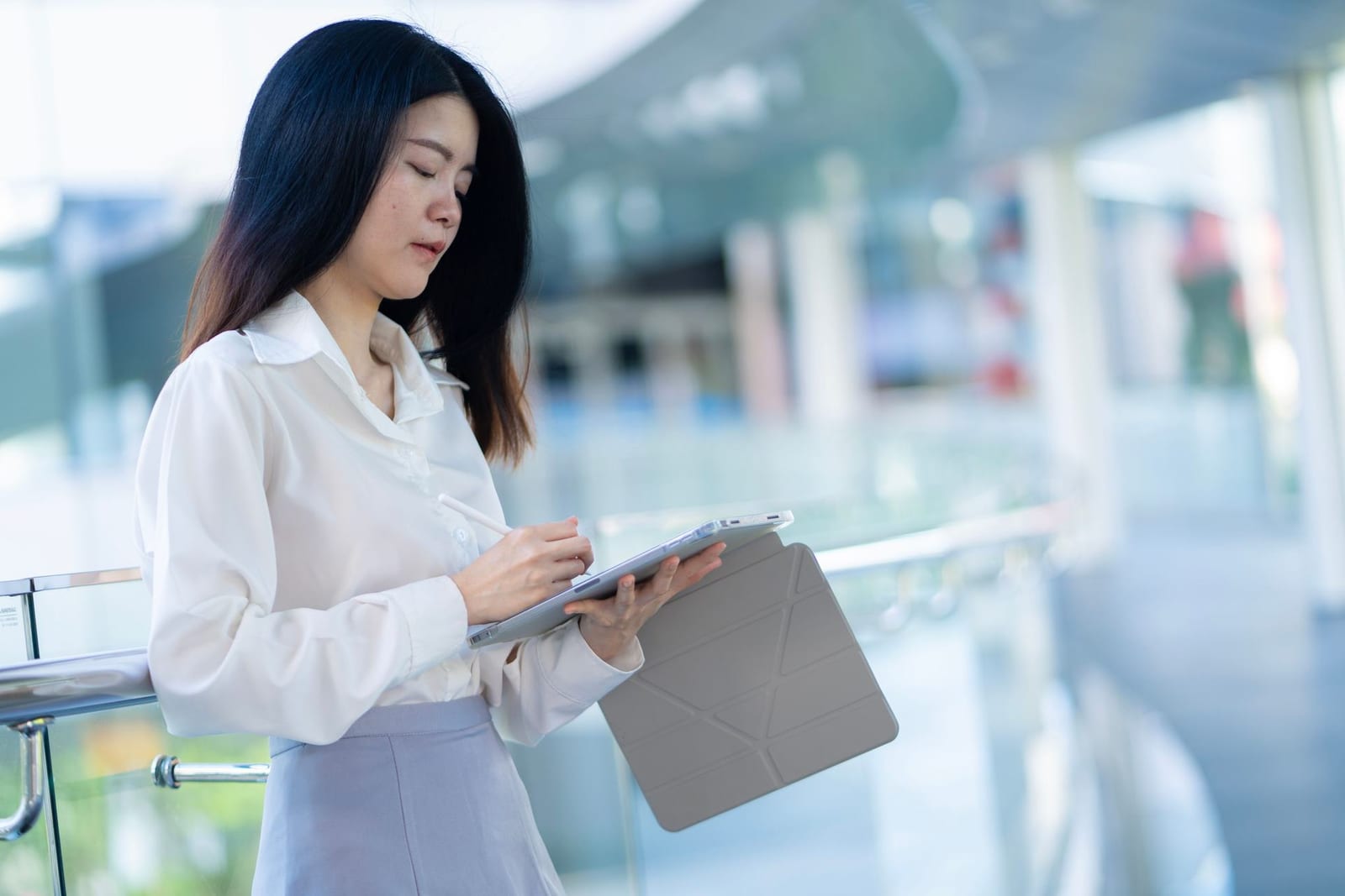 A clinician in a white blouse reviews notes on a tablet in a bright office atrium