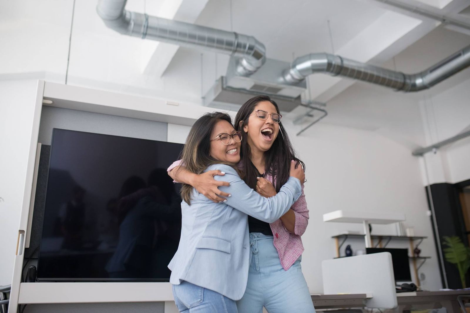 Two women in an office embrace and laugh together in celebration