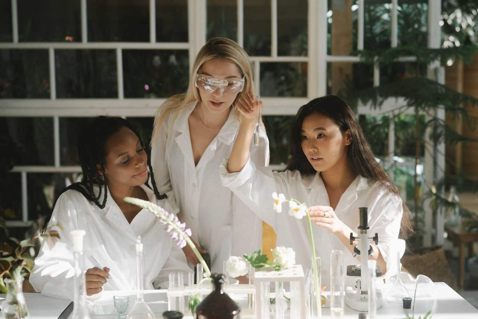 Three researchers in white lab coats examining flowering plant samples and test tubes on a bright lab bench, a generic stand-in for antibody-drug-conjugate research — not Medicovestor's own staff or labs