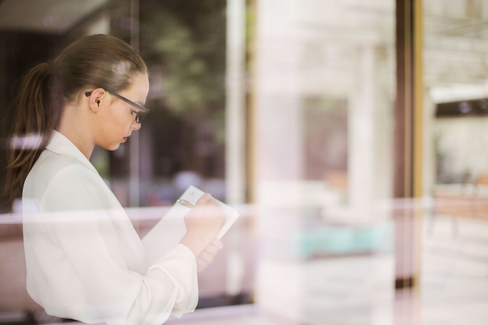 A clinician in a white blouse reviews notes reflected in a glass partition in a bright office