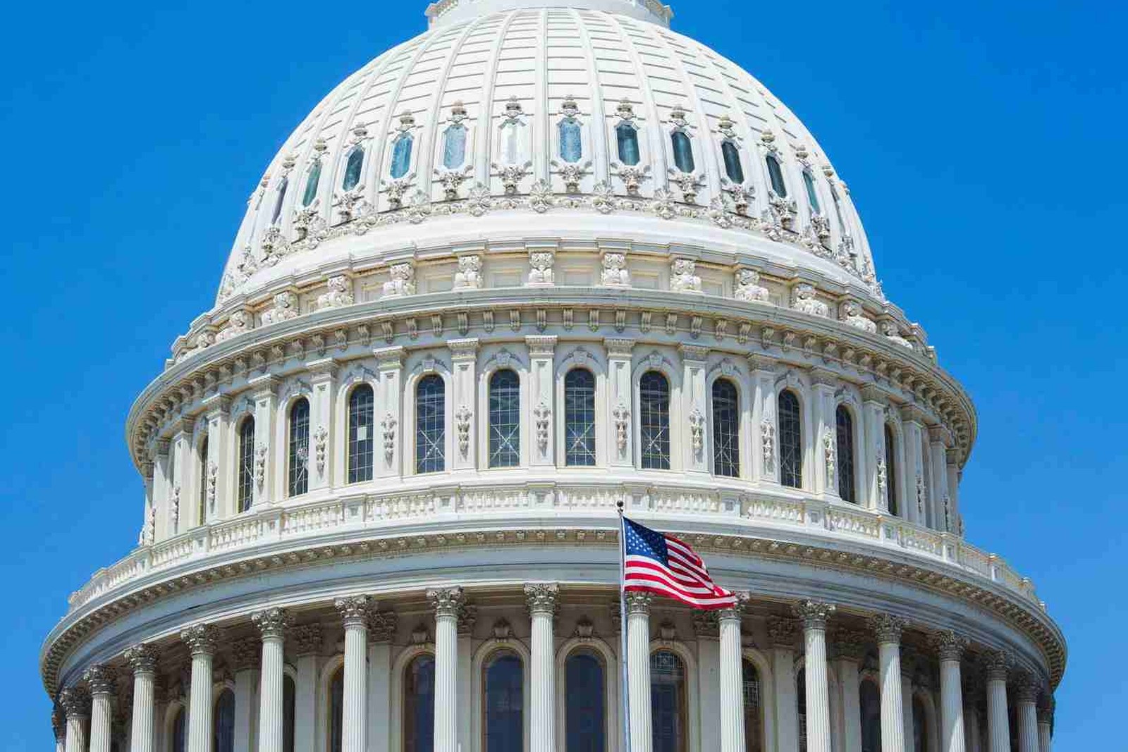 The dome of the U.S. Capitol rises against a clear blue sky, an American flag flying from its balustrade