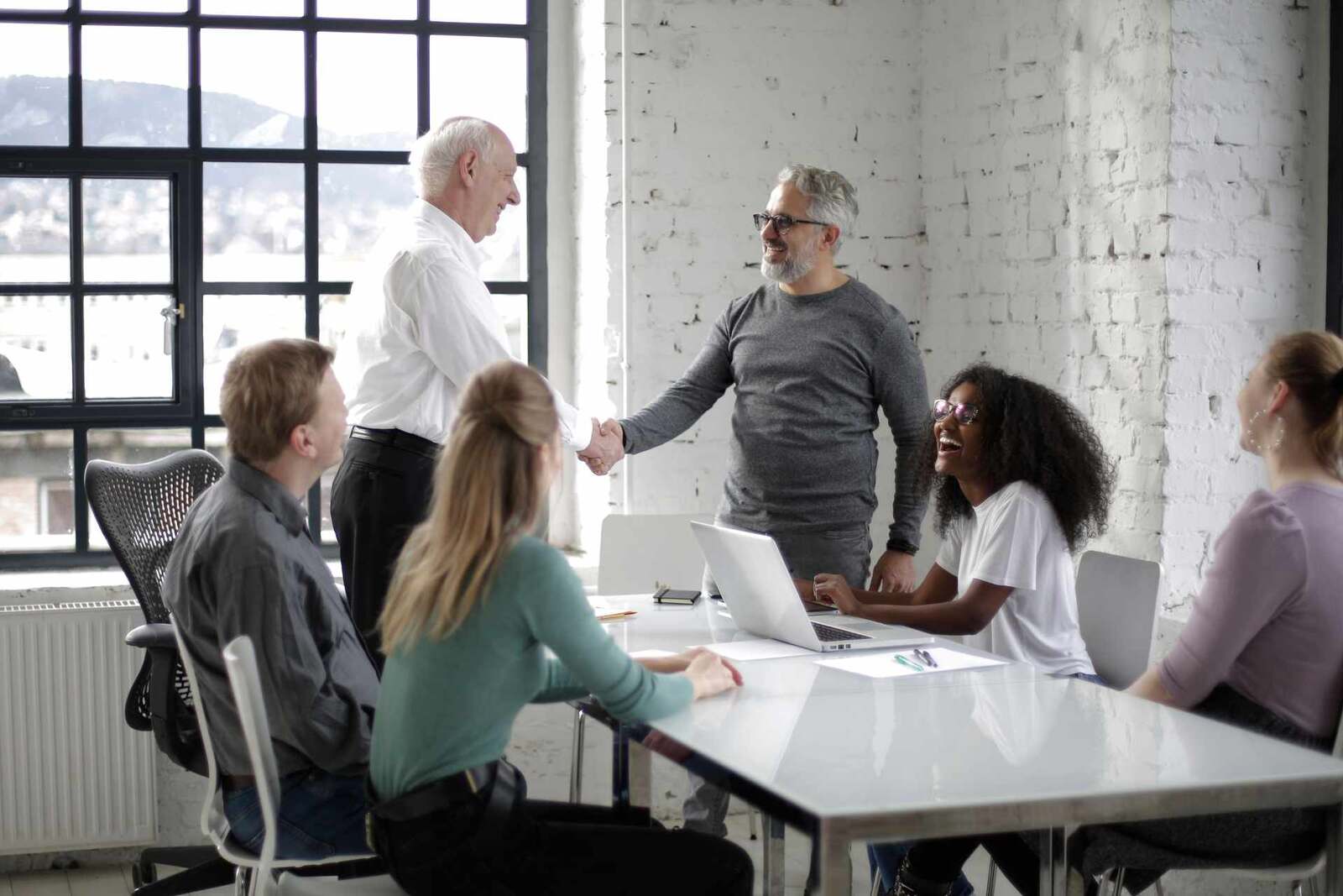 Colleagues shake hands around a conference table in a bright loft office